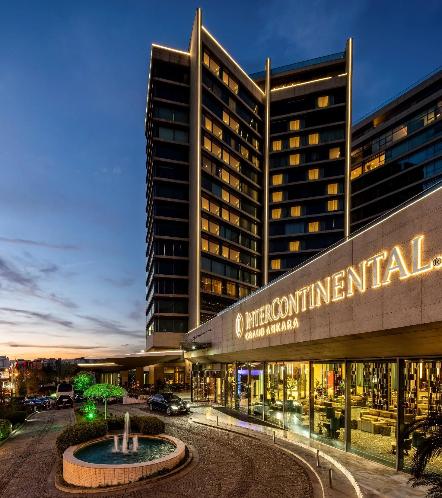 The InterContinental Grand Ankara tower lit up in the evening, with the entrance sign and the ornamental pool in front
